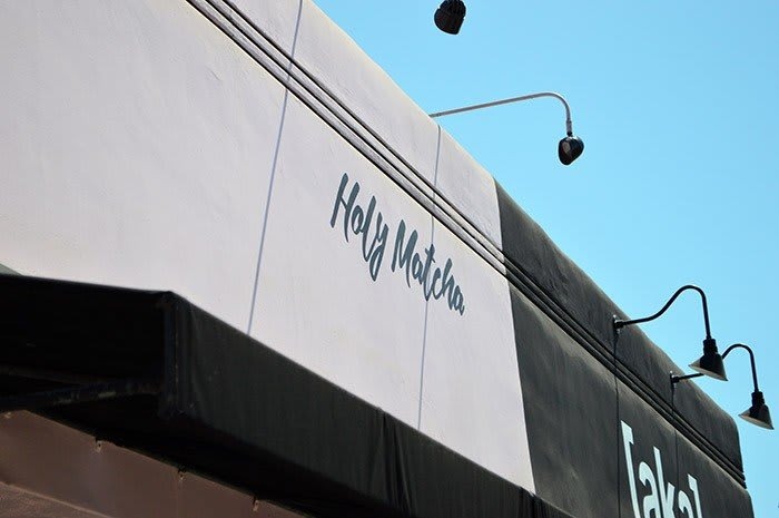 A sign reading "Holy Matcha" on a building exterior, with a clear blue sky in the background.
