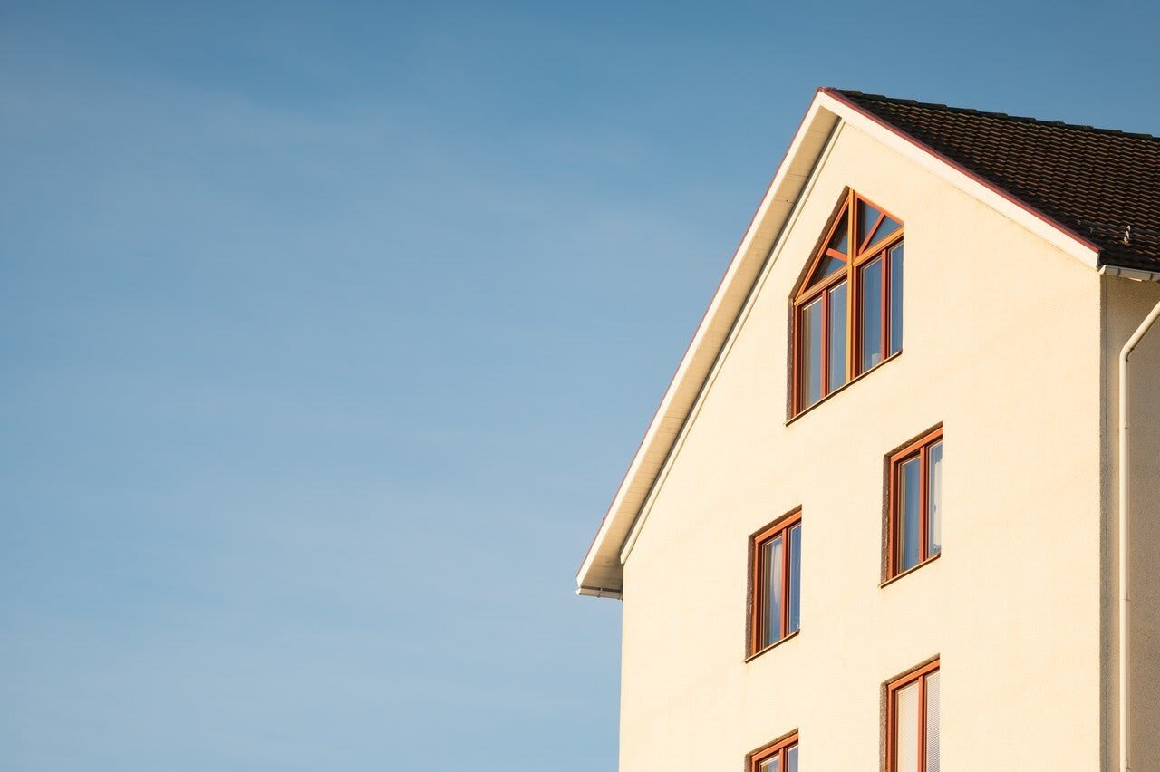 A close-up of a building's upper section featuring a sloped roof and multiple windows against a clear blue sky.