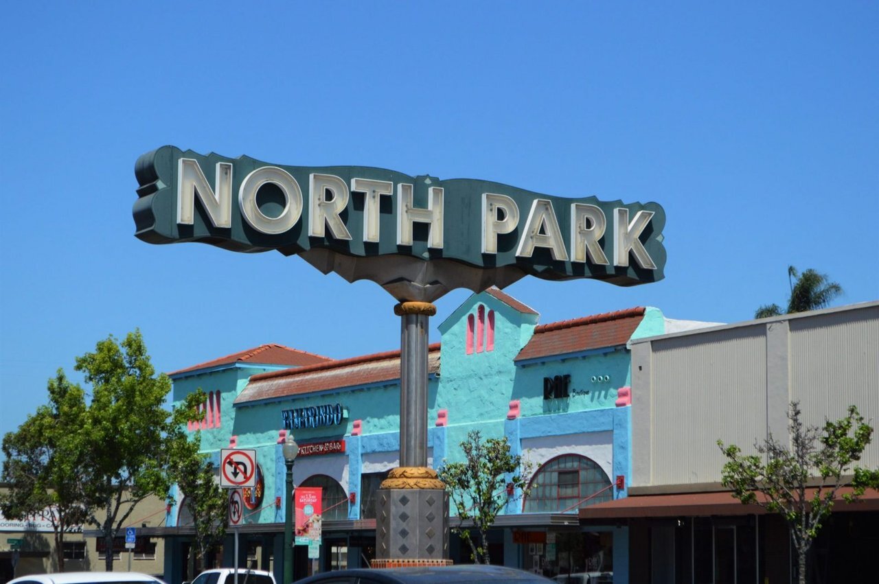 A colorful sign reading "NORTH PARK" stands prominently in front of buildings under a clear blue sky.